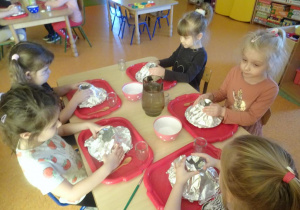 Piątka dzieci przygotowuje makietę wulkanu, do wykonania którego użyły talerzyka, kubka i folii aluminiowej.